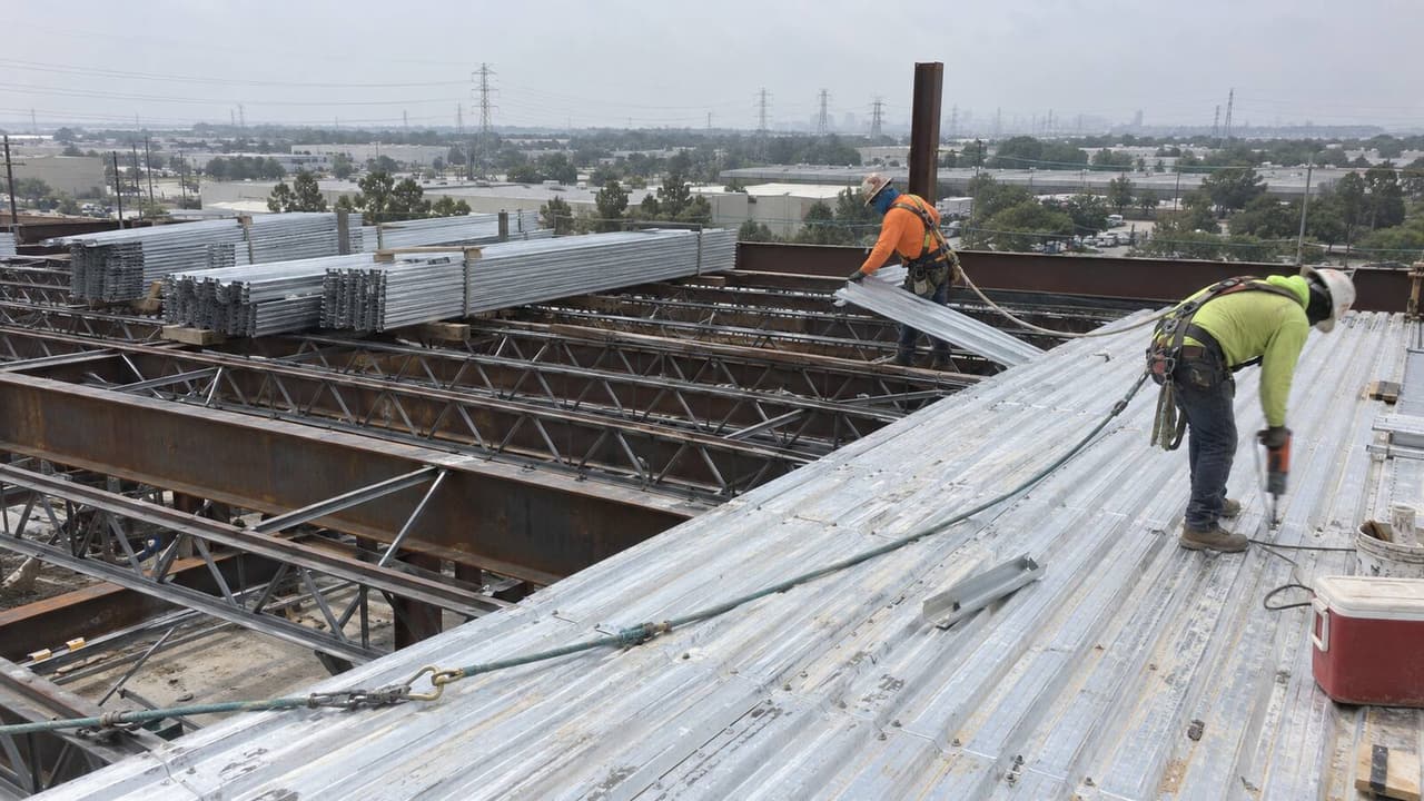 Ironworkers laying and fastening galvanized metal deck over steel bar joists on a Houston roof