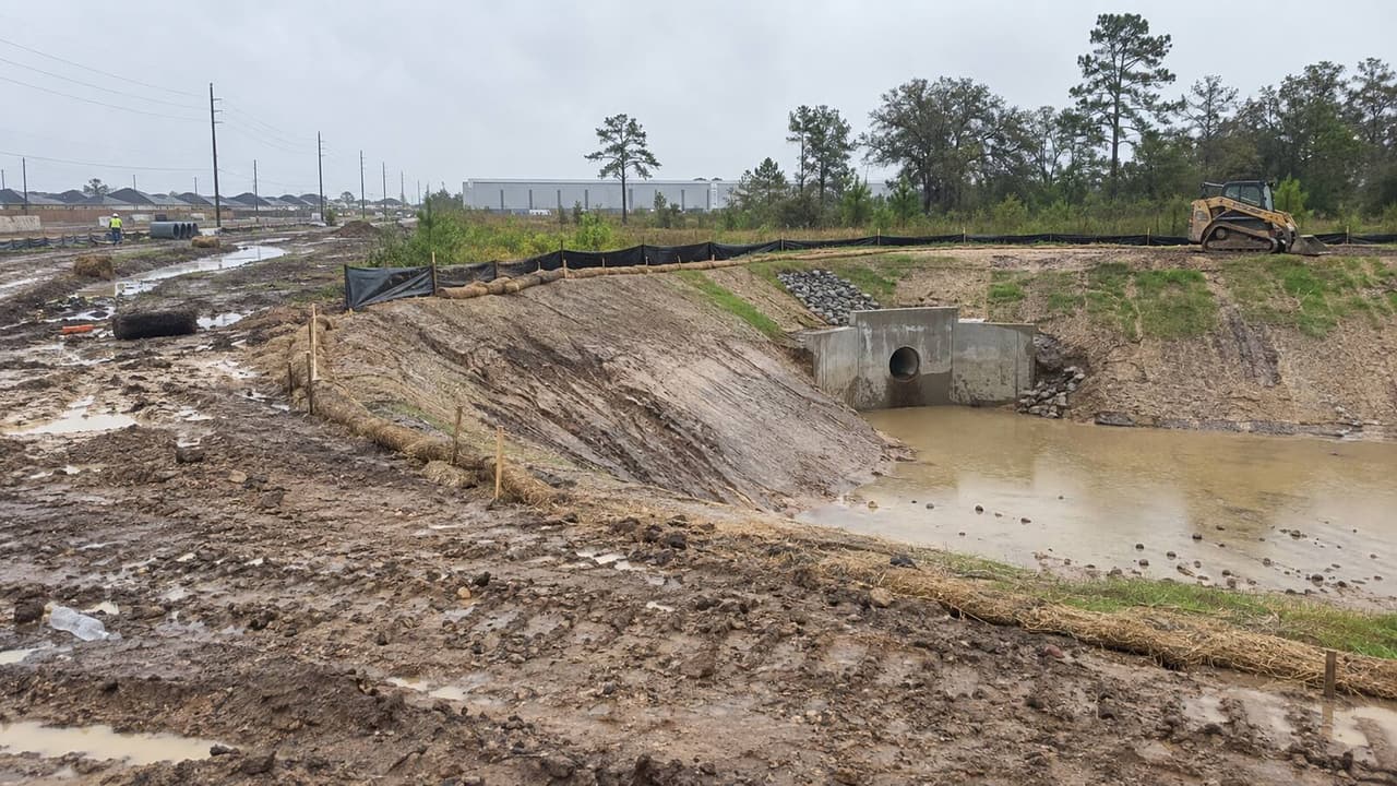 Newly cut detention pond with silt fence and a concrete outfall on a Houston development